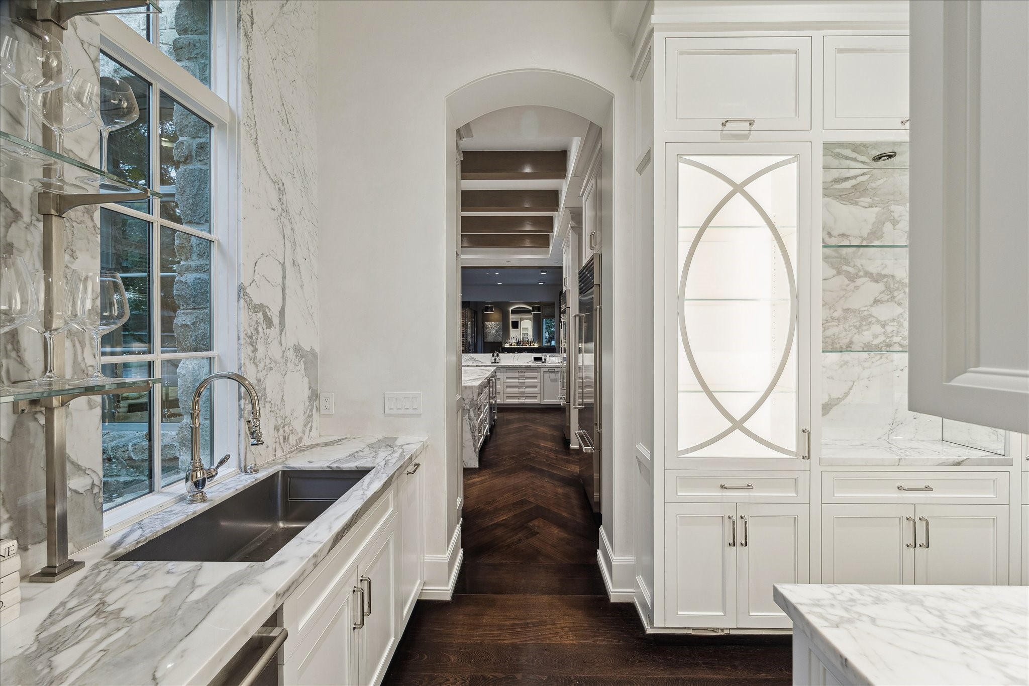 220 Merrie Way Lane Houston, TX 77024 - Photo 17 of 50 The butler’s pantry combines elegance and function with Calacatta marble countertops, full-height backsplash, and soft-close cabinetry. Glass-front display cabinets with LED lighting, floating shelves, and under-cabinet illumination highlight a polished nickel sink and fixtures, completing this refined prep and service space.