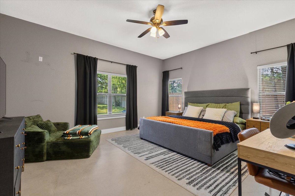 145 Cardinal Loop Paige, TX 78659 - Photo 20 of 40 Well-lit and tranquil, this primary bedroom retreat features elegant concrete flooring and multiple windows framing verdant exterior views.