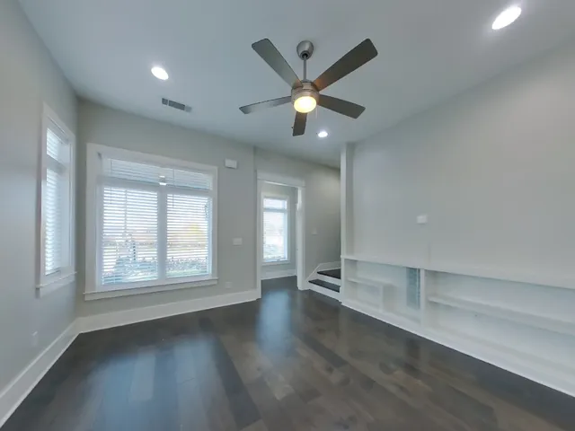an empty room with wooden floor fan and windows