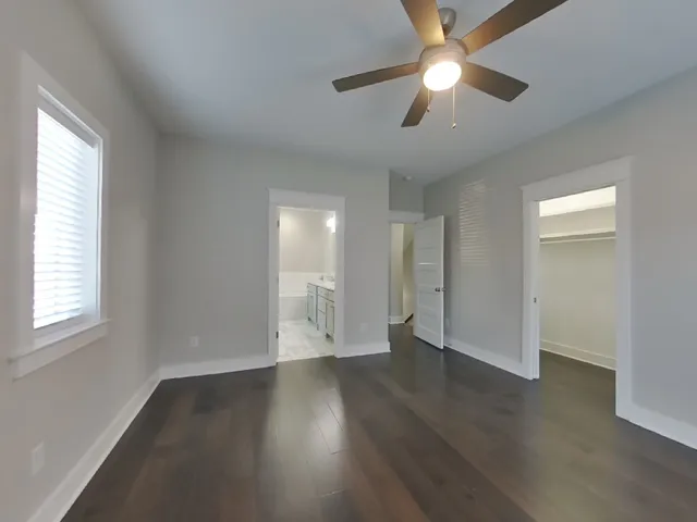 an empty room with wooden floor chandelier fan and windows