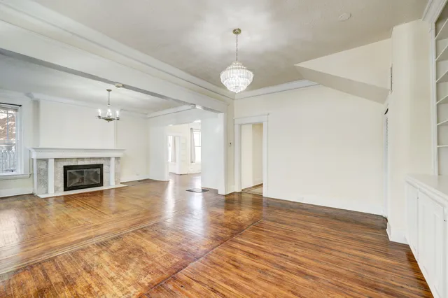 a view of an empty room with wooden floor fireplace and a window