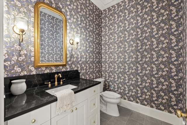 478 South Maple Lakes Drive Mapleton, UT 84664 - Photo 29 of 51 Powder room featuring floral wallpaper, a white vanity with gold hardware, a black countertop, gold-finish wall sconces, and a gold-framed mirror