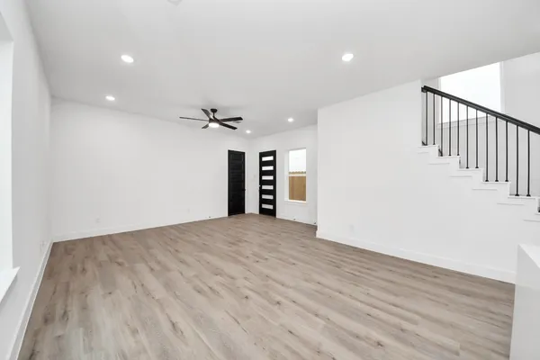 a view of an empty room with wooden floor and a ceiling fan