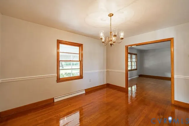 an empty room with wooden floor chandelier and windows