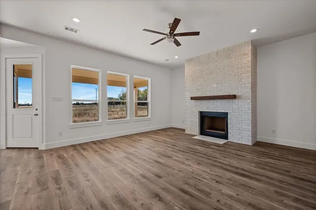 a view of an empty room with wooden floor fireplace and a window