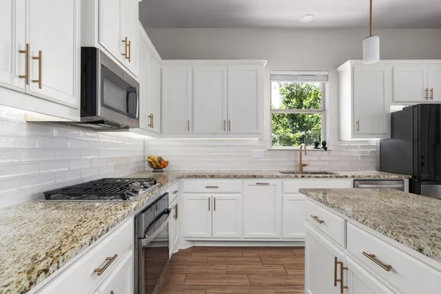 a kitchen with granite countertop stainless steel appliances white cabinets sink and window