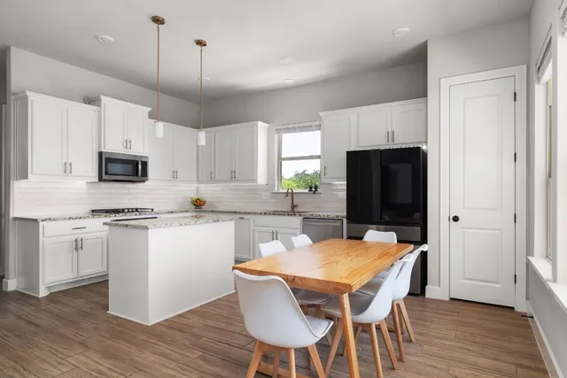 a kitchen with stainless steel appliances granite countertop a stove a sink a microwave a refrigerator and white cabinets with wooden floor