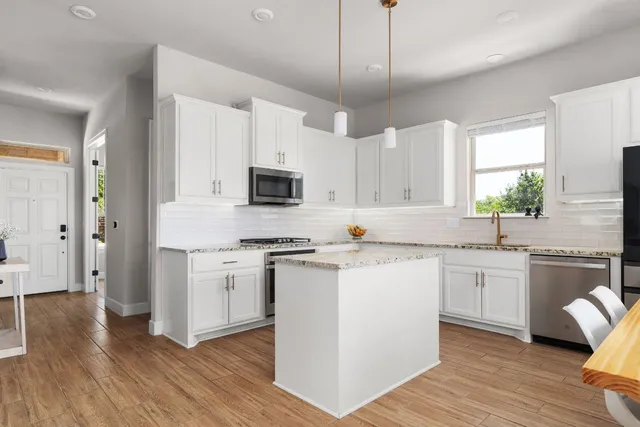 a kitchen with stainless steel appliances granite countertop a sink a stove a refrigerator and white cabinets with wooden floor