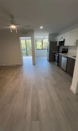 a view of an empty room with kitchen and window