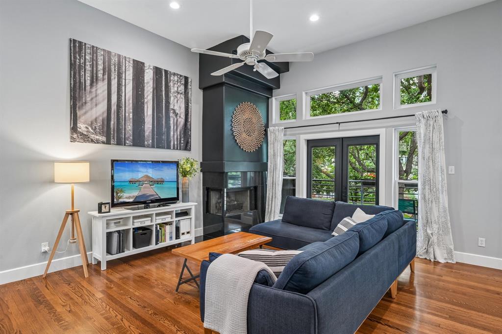 3553 Wheeler Street Dallas, TX 75209 - Photo 6 of 35 Living room featuring soaring ceilings, statement fireplace with dark accent wall, and French door balcony access with tree canopy views