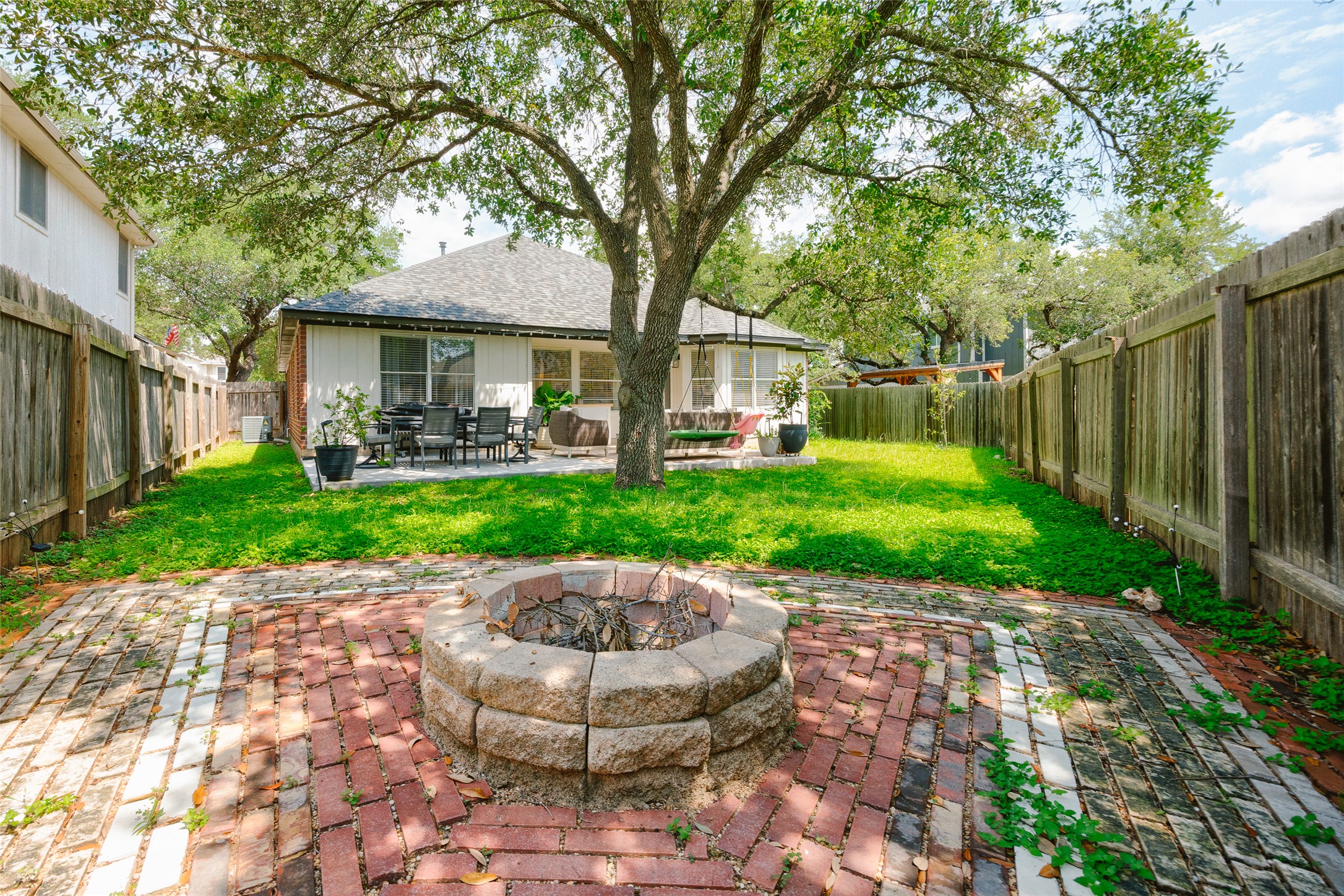 2202 Old Mill Road Cedar Park, TX 78613 - Photo 20 of 23 An inviting backyard features a brick patio, a built-in fire pit, and lush green lawn beneath mature shade trees.