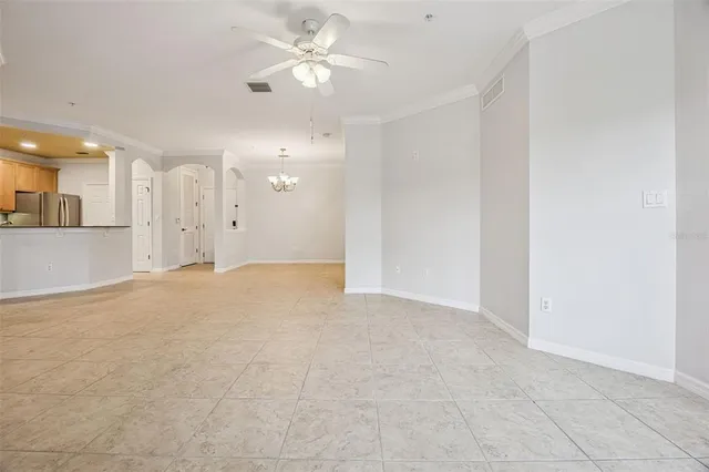 an empty room with kitchen view and a ceiling fan