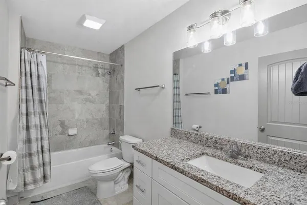 a bathroom with a granite countertop sink a toilet a mirror a bathtub and shower