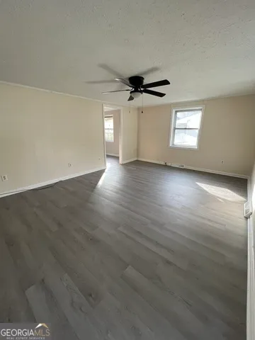 an empty room with wooden floor ceiling fan and windows