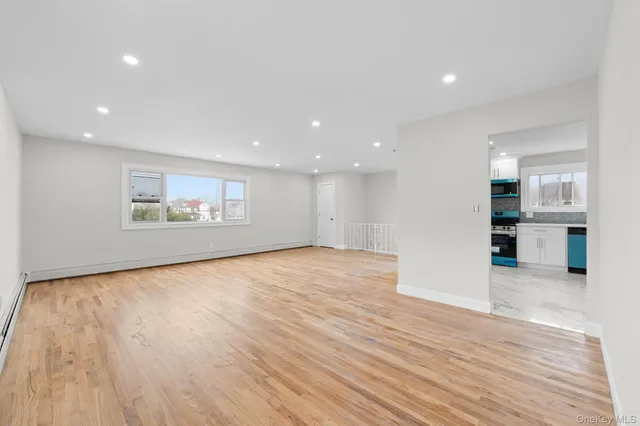 a view of an empty room with wooden floor and a kitchen