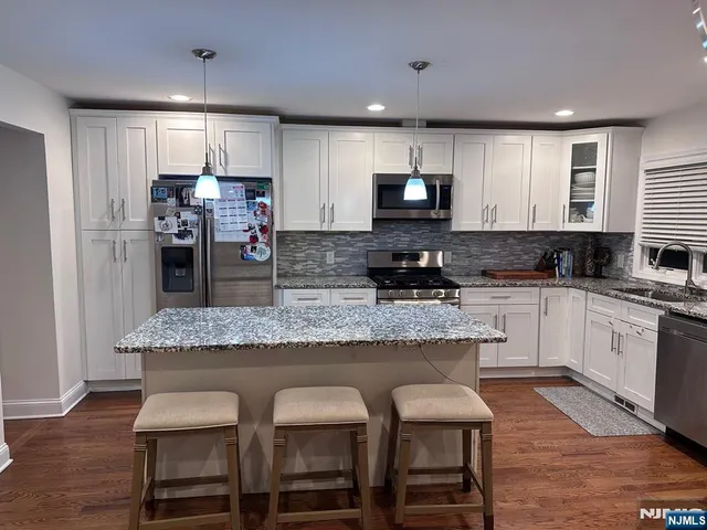 a kitchen with stainless steel appliances granite countertop a stove top oven a sink a refrigerator and white cabinets