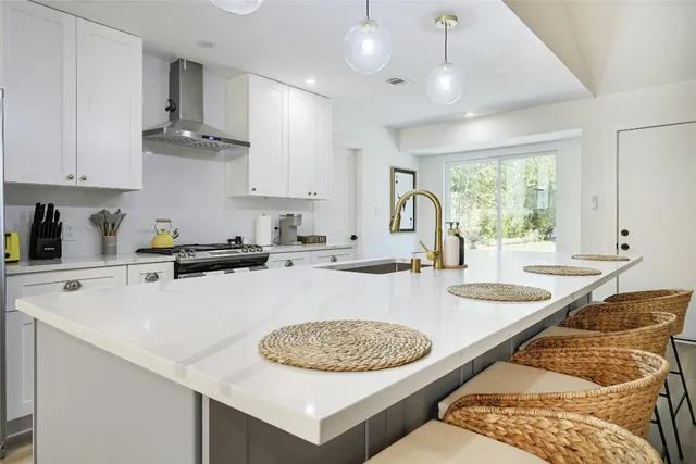 a kitchen with stainless steel appliances granite countertop a sink a stove a kitchen island with chairs and white cabinets