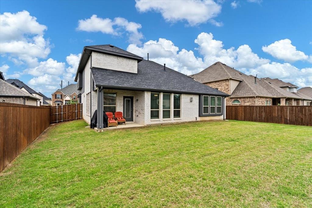620 Shadow Trail Frisco, TX 75033 - Photo 32 of 36 Expansive grassy backyard featuring a full privacy fence, covered patio, and multiple large windows with dark trim