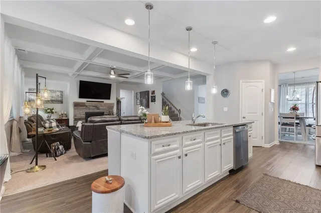 a kitchen with kitchen island granite countertop a sink a stove a refrigerator and white cabinets with wooden floor