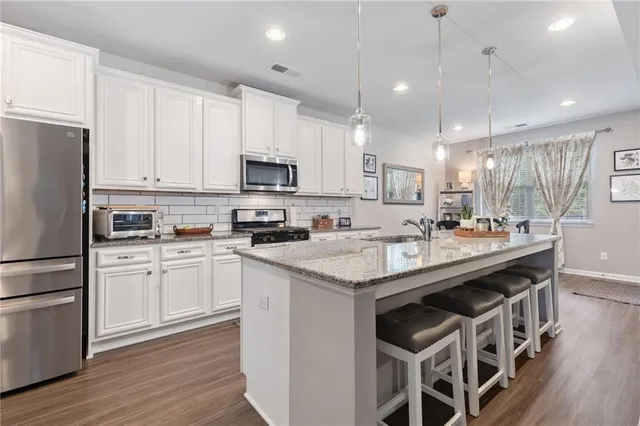 a kitchen with stainless steel appliances granite countertop a stove a sink dishwasher and a refrigerator with white cabinets