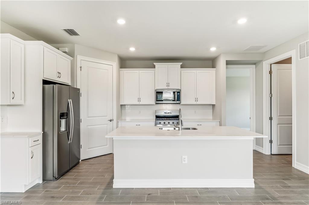 17788 Shade Tree Loop Punta Gorda, FL 33982 - Photo 6 of 44 Kitchen featuring wood tiled floors, appliances with stainless steel finishes, recessed lighting, white cabinets, and a center island with sink