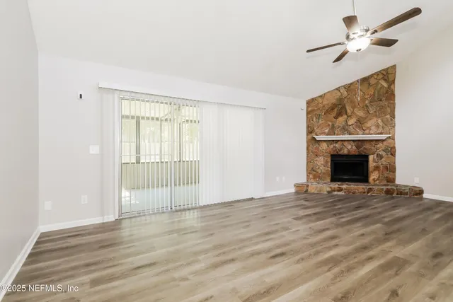 a view of an empty room with wooden floor fireplace and a window