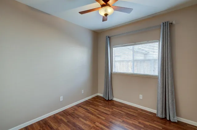 an empty room with wooden floor fan and windows