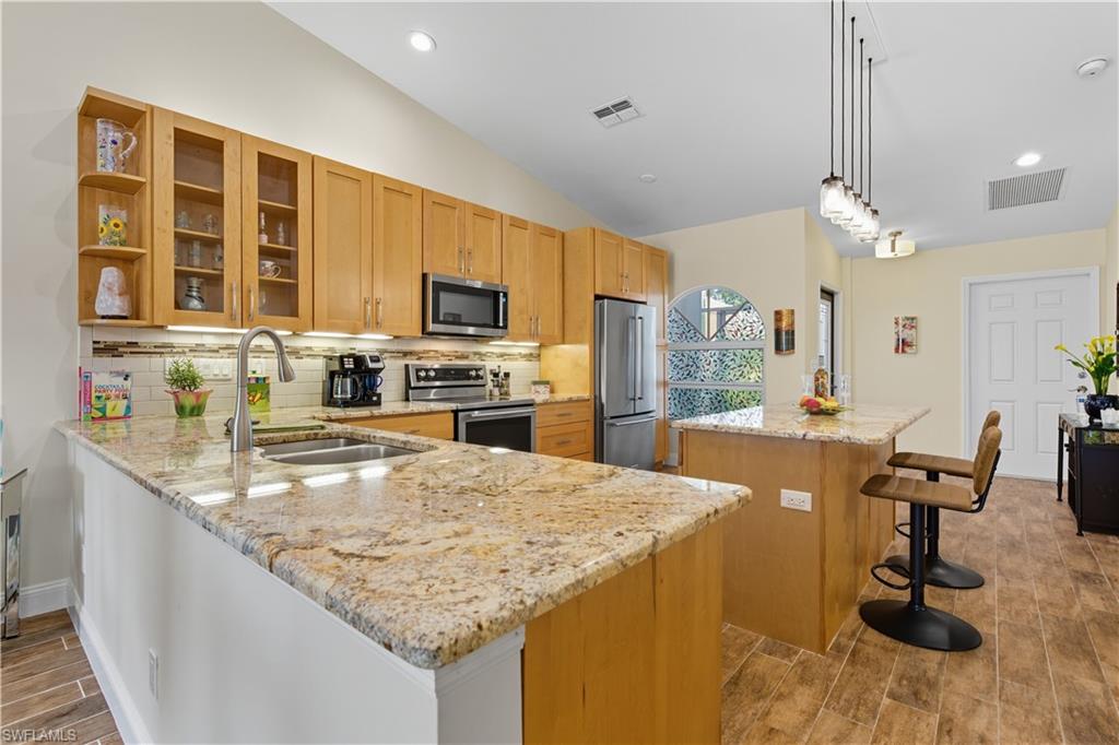 2266 Stacil Circle, Unit 3 Naples, FL 34109 - Photo 9 of 49 Kitchen with wood tiled floors, glass insert cabinets, backsplash, a center island, and light stone counters