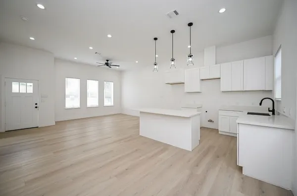 a large kitchen with stainless steel appliances a large counter top a sink a refrigerator and white cabinets with wooden floor