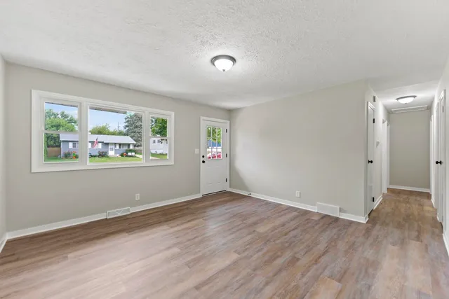 a view of an empty room with wooden floor and a window