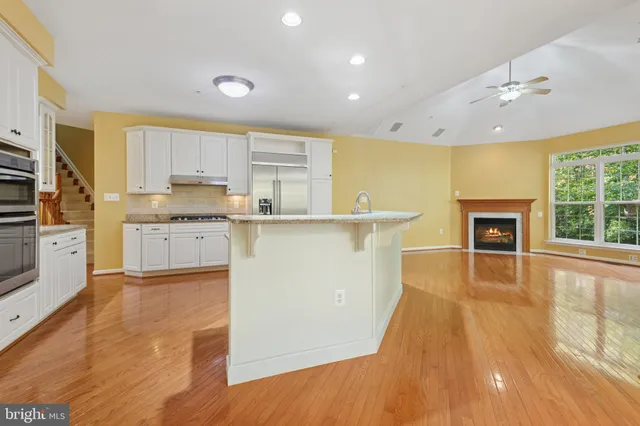 a kitchen with stainless steel appliances granite countertop a refrigerator a sink dishwasher and a fireplace with wooden floor