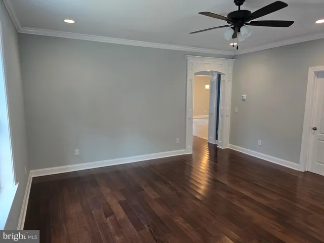 a view of an empty room with wooden floor and a ceiling fan