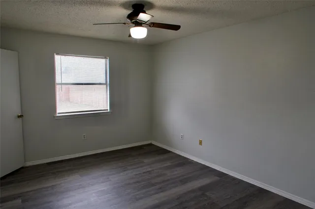 an empty room with wooden floor chandelier fan and windows