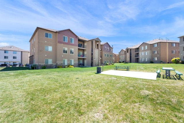 8215 Clear Rock Road, Unit 12 Eagle Mountain, UT 84005 - Photo 35 of 38 Expansive green space featuring a concrete patio with picnic tables, surrounded by multi-story residential buildings