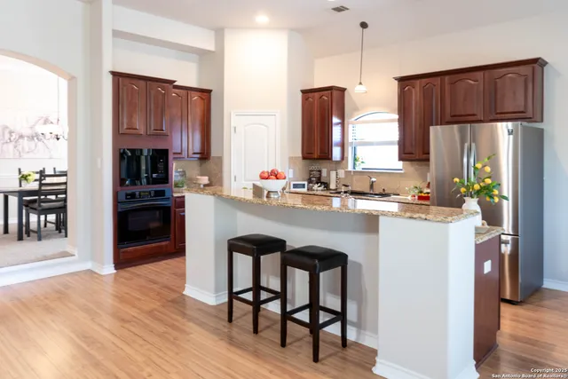 a kitchen with stainless steel appliances granite countertop a refrigerator a stove a sink a dining table and chairs with wooden floor