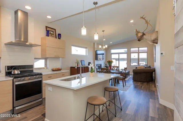 a open kitchen with kitchen island a stove a sink a dining table and chairs with wooden floor