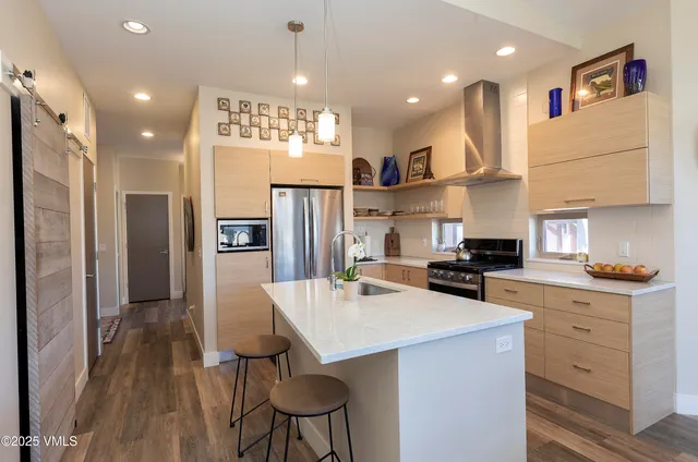 a kitchen with stainless steel appliances kitchen island granite countertop a refrigerator a stove a sink a dining table and chairs with wooden floor
