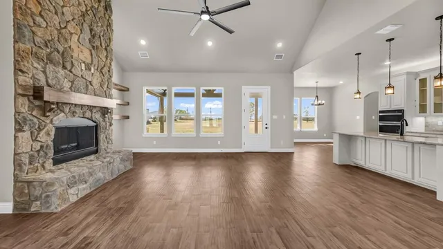 an empty room with wooden floor fire place and kitchen view
