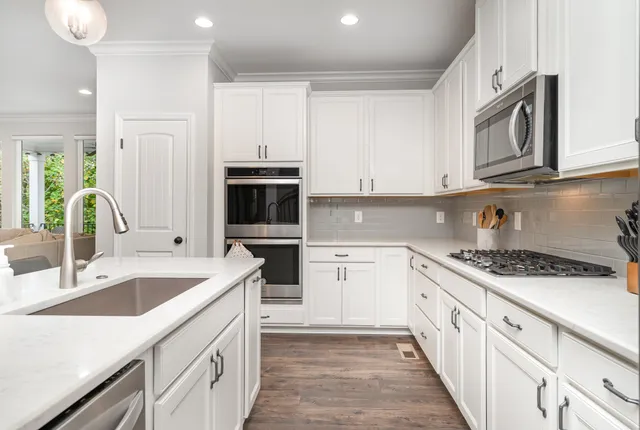 a kitchen with stainless steel appliances granite countertop a sink stove oven and white cabinets with wooden floor