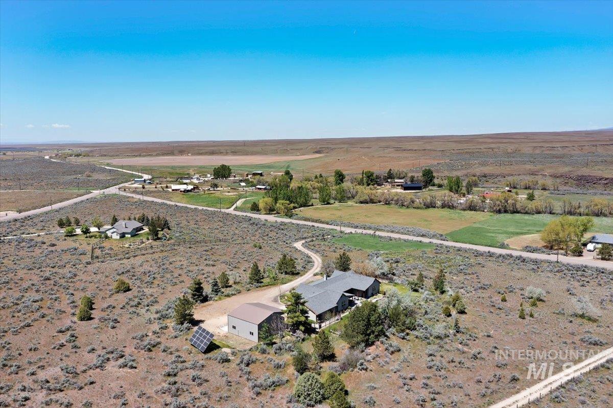 147 East Indian Crk Road Boise, ID 83716 - Photo 43 of 43 Expansive property featuring a single-story residence with a dark gray roof, a detached metal outbuilding, a visible solar panel array, a winding gravel driveway, and surrounding arid landscaping with mature trees