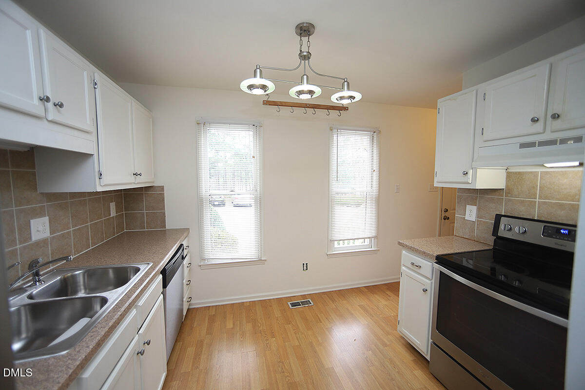 6514 Hearthstone Drive Raleigh, NC 27615 - Photo 4 of 16 a kitchen with stainless steel appliances a sink dishwasher stove and white cabinets with wooden floor