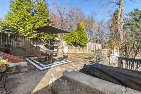 a view of a patio with table and chairs under an umbrella with large trees