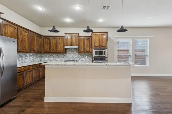 a kitchen with stainless steel appliances kitchen island granite countertop a refrigerator a sink and wooden cabinets