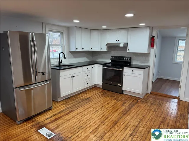 a kitchen with granite countertop a refrigerator a sink and wooden floors