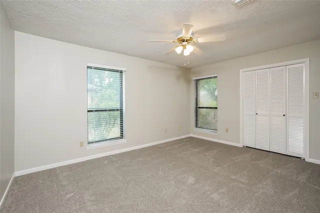 an empty room with chandelier fan and windows