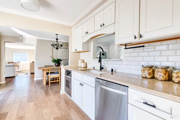 a kitchen with a sink dishwasher stove and white cabinets with wooden floor