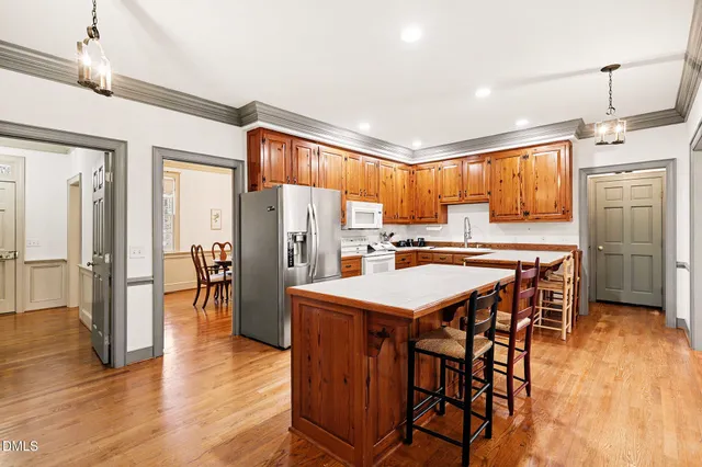 a kitchen with stainless steel appliances kitchen island granite countertop a refrigerator a stove a sink a dining table and chairs with wooden floor