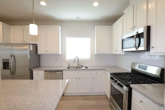 a kitchen with stainless steel appliances granite countertop a sink a stove a refrigerator cabinets and white cabinets