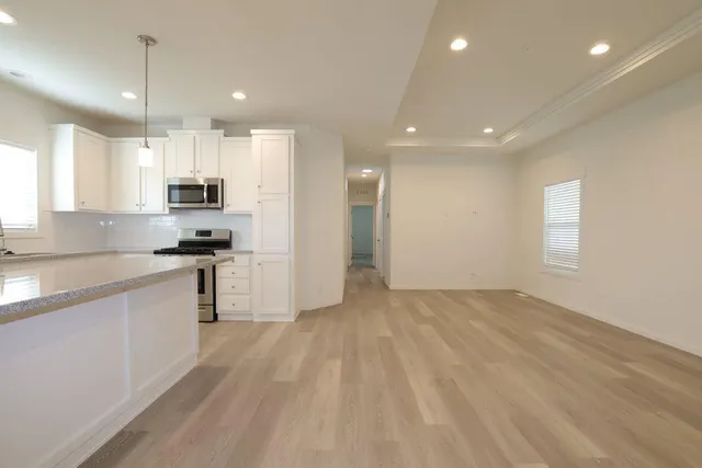 a open kitchen with kitchen island a sink dishwasher a refrigerator and white cabinets with wooden floor