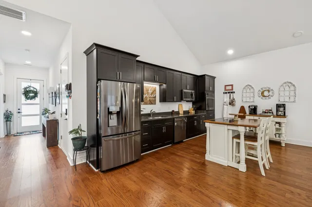 a kitchen with stainless steel appliances a refrigerator a stove a sink a dining table and chairs with wooden floor